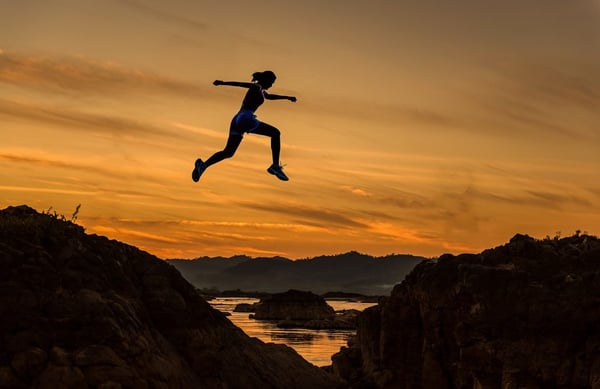 Person jumping between mountains as symbol of success or failure