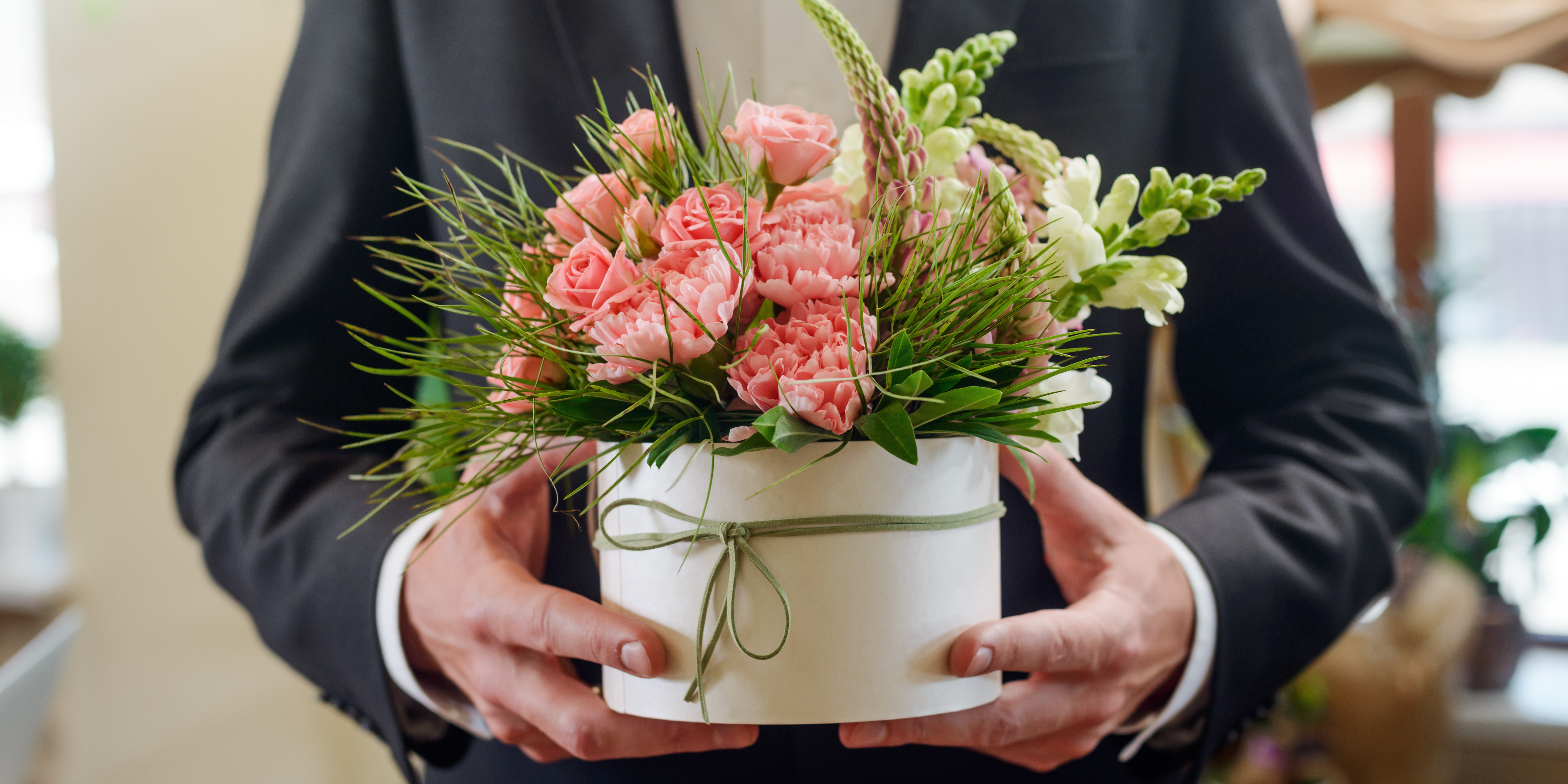 A man in suit carrying a pot of pink flowers